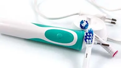 Teal and white electric toothbrush with two replacement brush heads and a white charging station.