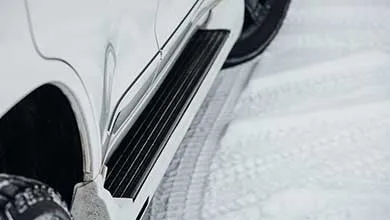 Close-up of a white vehicle's black, ridged running board, with tire tracks in the snow.