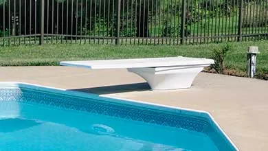 White diving board extending over a blue swimming pool from a concrete deck.