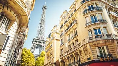 The Eiffel Tower centered between two ornate stone apartment buildings under a clear sky.