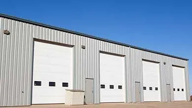 Corrugated metal building with three white roll-up garage doors under a clear sky.