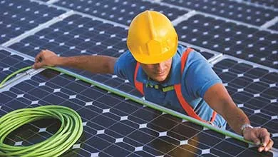 Technician installing or measuring solar panels on a large solar array using a green cable.