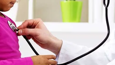 Healthcare professional using a stethoscope to examine a seated child in a clinical room.
