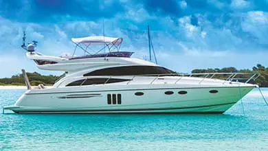 A large white yacht anchored in calm turquoise water beneath a cloudy blue sky.