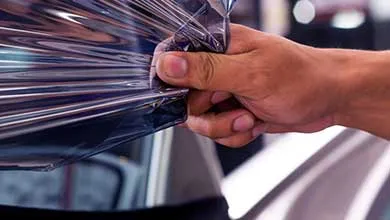 Close-up of a hand holding a creased, glossy sheet of transparent plastic film reflecting light.