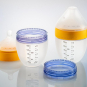 Two baby bottles and their parts on a reflective surface. One bottle is fully assembled with a yellow ring; the other is disassembled, showing a milk-filled container beside its purple and blue rings.